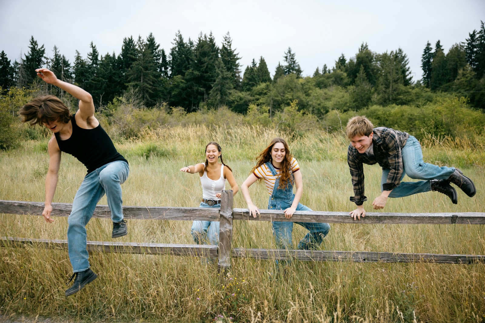 Four friends climbing over a wooden fence outdoors